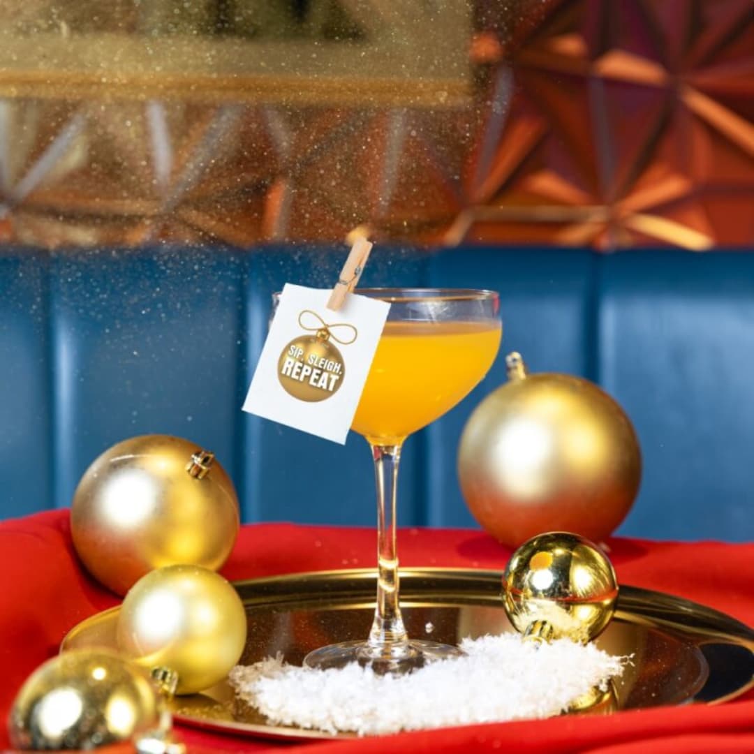 Orange cocktail in coupe glass surrounded by baubles